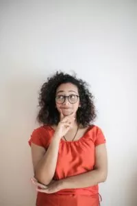 אישה מטולטלת עם משקפיים חושבת, היא שמה את היד שלה על הסנטר ומסתכלת לצד ימין של התמונה